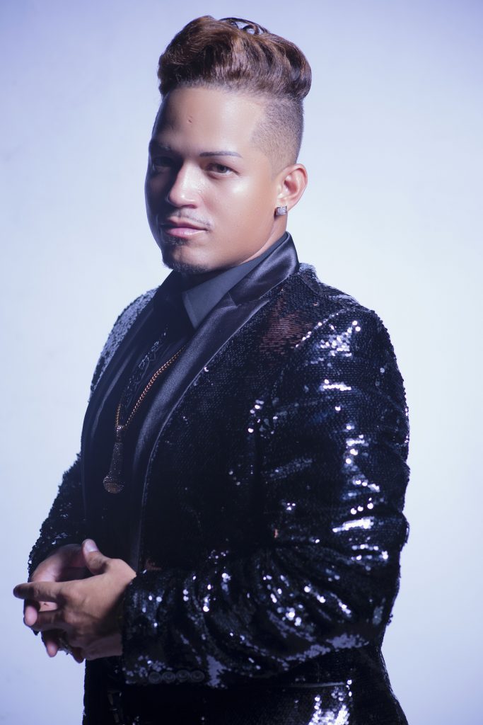 A stylish individual poses confidently in a sparkling black sequined blazer, set against a soft blue background.